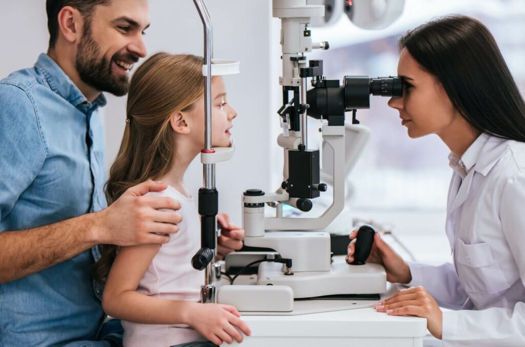 A young child sitting on their parent's lap during an eye exam while an optometrist looks for signs of myopia.