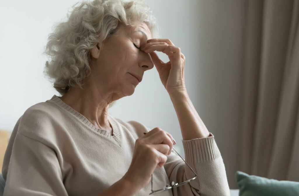 Older woman with age-related macular degeneration sitting with eyes closed, hand resting gently at the corners of her eyes.