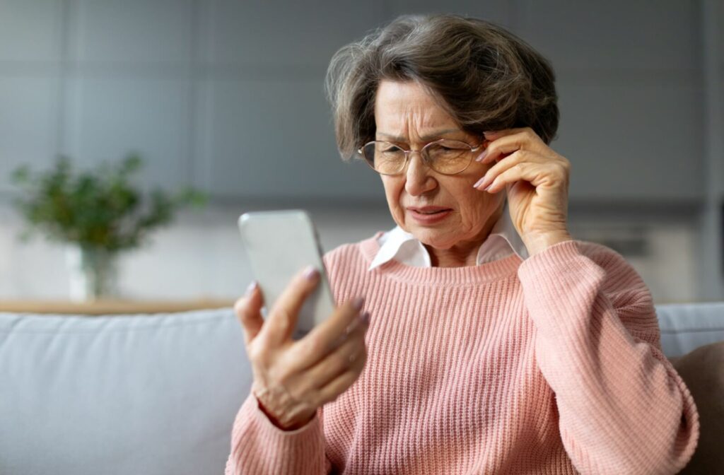 Senior person squinting at smartphone while adjusting her glasses.