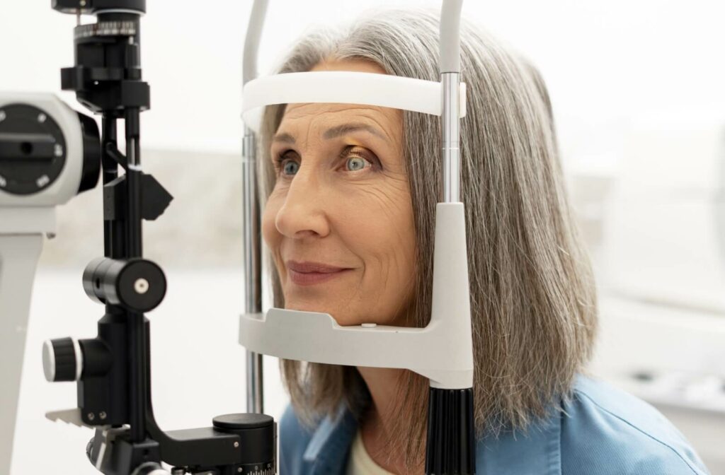 Senior person undergoing an eye exam, seated at a slit lamp machine with her chin and forehead resting on the support.