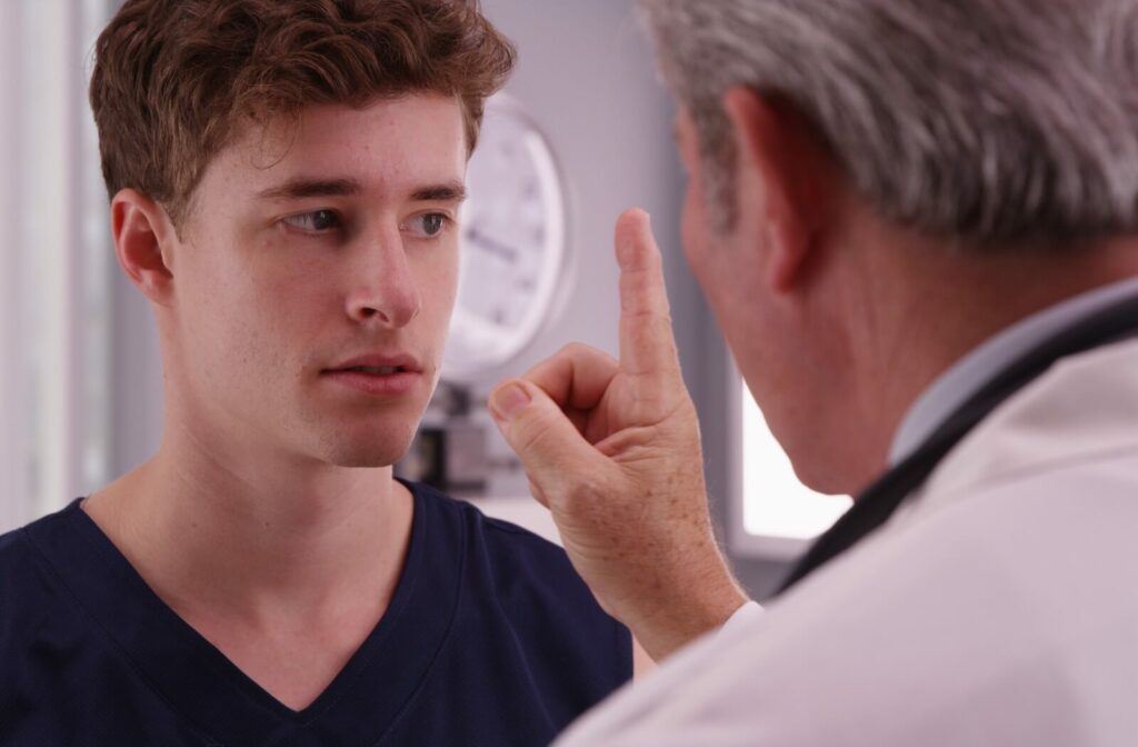 Doctor performs an eye movement test on a young male patient, holding up a finger for the patient to follow.