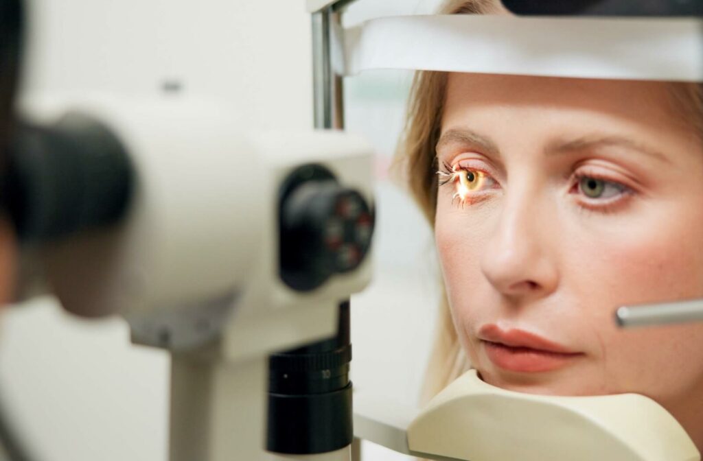 Person sitting at a slit-lamp machine during an eye exam, with a bright light shining into one eye as they rest their chin on the support.