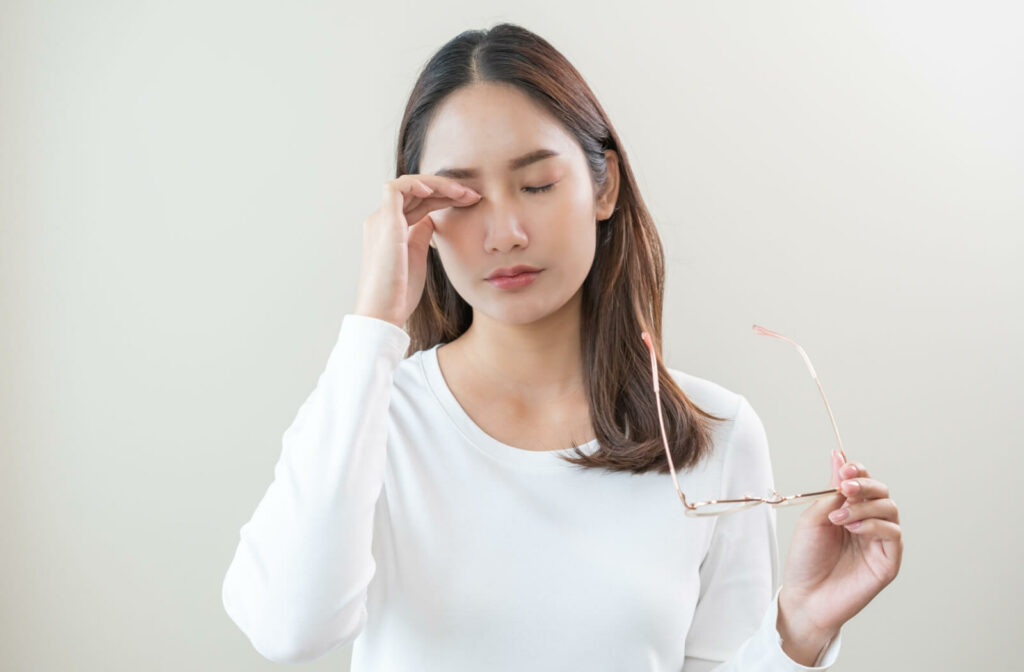 A woman removing her glasses and rubbing her tired, irritated eyes, illustrating common symptoms of chronic dry eye syndrome.