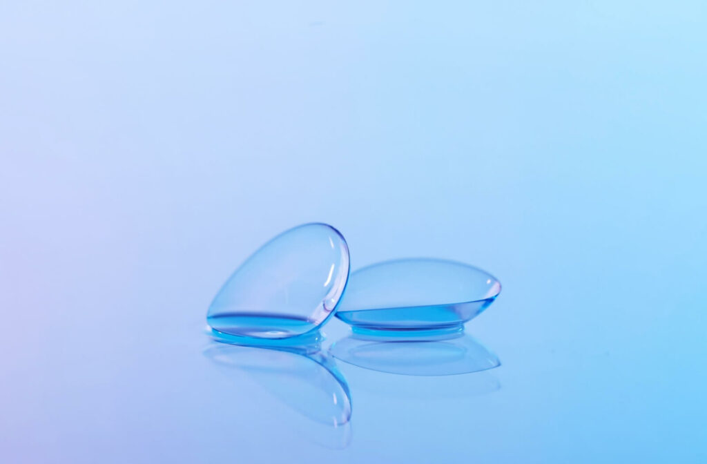 Two clear contact lenses resting on a reflective blue surface, illustrating an alternative to sports glasses for vision correction.